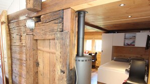 L’intérieur d’un chalet rustique, avec une grande porte en bois, un poêle à bois central, un lit doté d’une tête de lit et un coin repas.