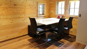 Une pièce aux murs lambrissés, avec une table et quatre chaises, deux fenêtres et une radio rouge.