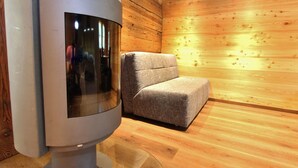 Une pièce moderne avec un grand radiateur cylindrique, un fauteuil recouvert d’un tissu gris et des murs en bois.