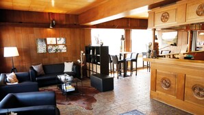 A spacious living area with a sofa, coffee table, and a rug. There is a dining area with chairs and a table. The room has wooden walls and a tiled floor. - Plush Apartment in Bollendorf with Sauna near Luxembourg (Bollendorf)