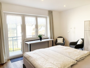 A bedroom with a bed, two chairs, a desk, and a window with curtains.