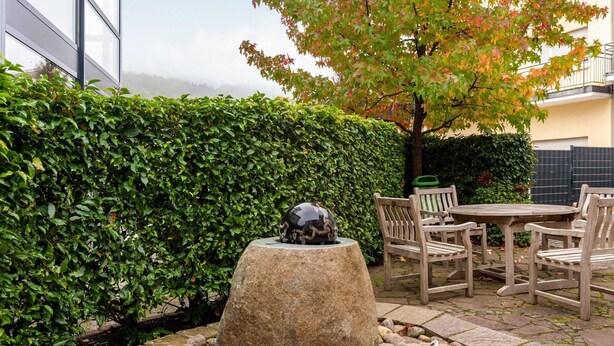 A patio area with a stone fountain, wooden chairs, and a table. - Plush Apartment in Bollendorf with Sauna near Luxembourg (Bollendorf)