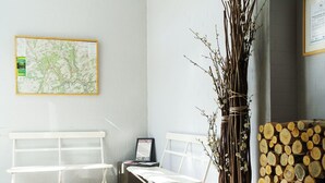 A room with a white bench, a small table, a map on the wall, and a vase of branches. - Plush Apartment in Bollendorf with Sauna near Luxembourg (Bollendorf)