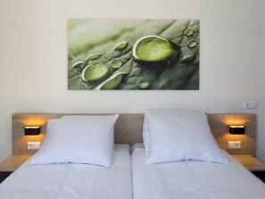 Ett hotellrum med en säng, två sänglampor och en tavla på väggen som föreställer vattendroppar på ett löv.
