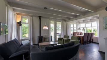 A spacious living room with a sofa, a dining table with chairs, and large windows providing natural light.