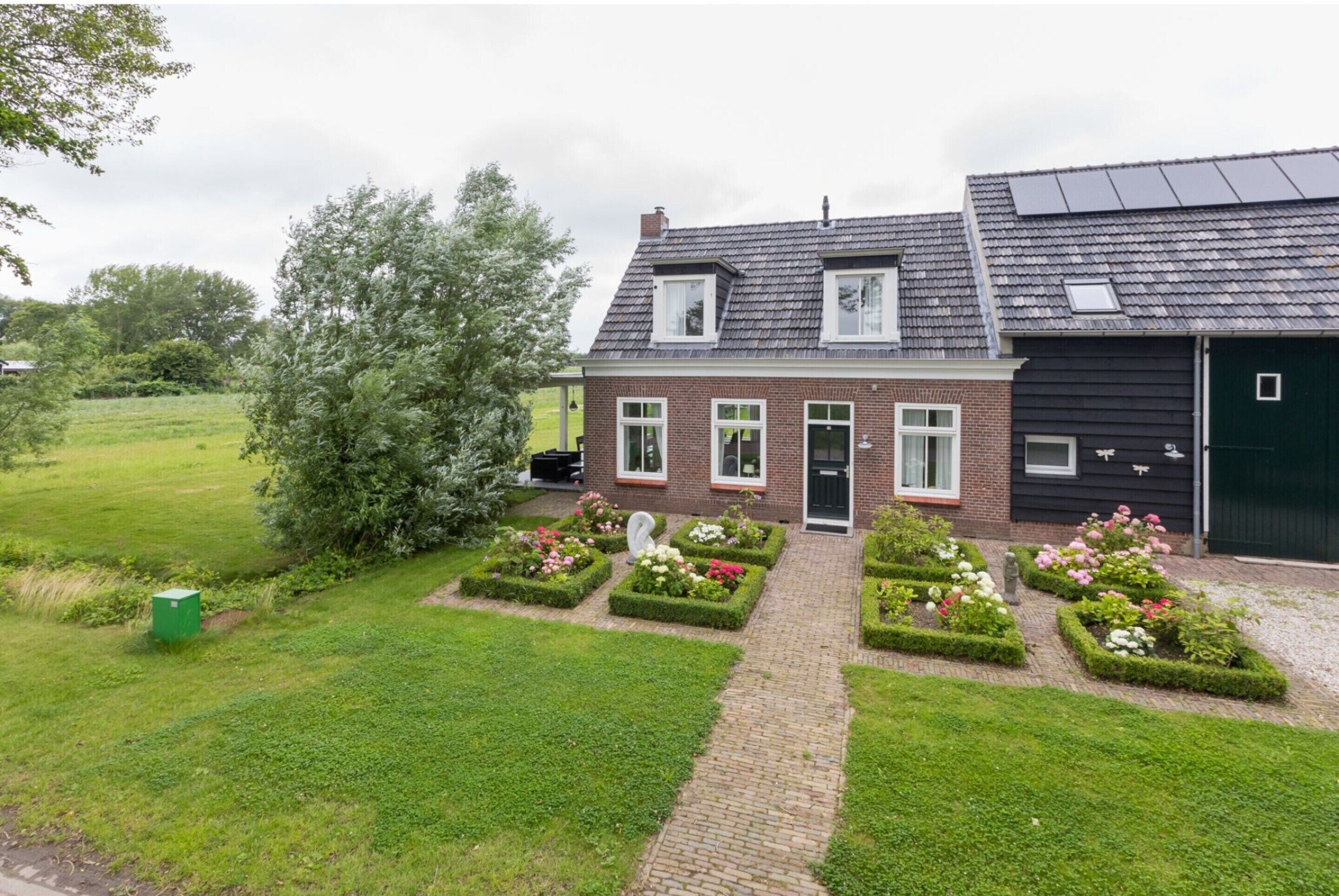 A two-story house with a brick facade, a black garage, and a garden with flower beds.