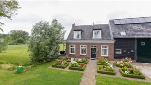 Ett tvåvåningshus med en fasad av tegel, ett svart garage och en trädgård med blomsterrabatter.