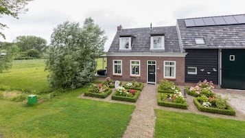 A two-story house with a brick facade, a black garage, and a garden with flower beds.