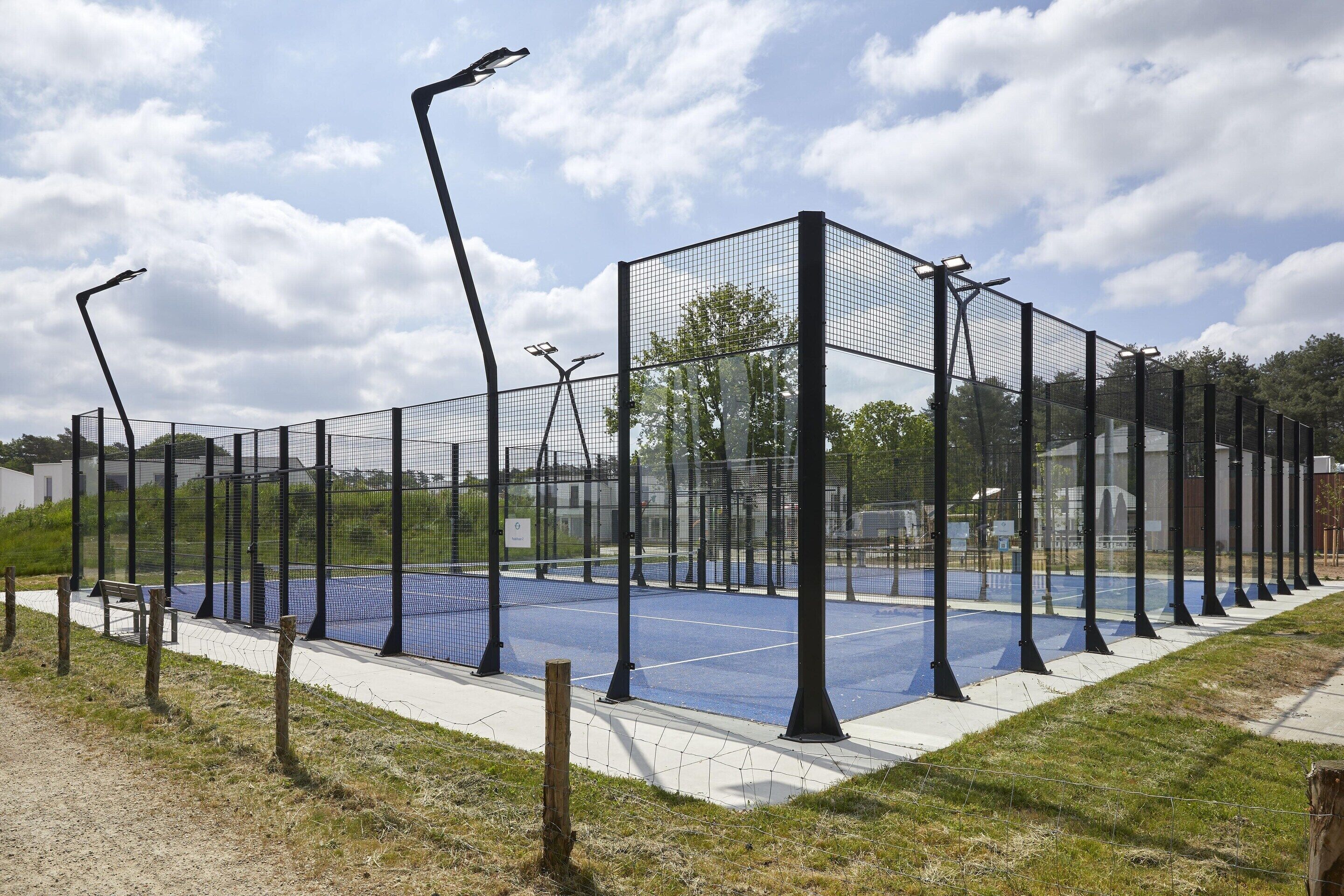 A tennis court enclosed by a black fence with a bench and street lamps.