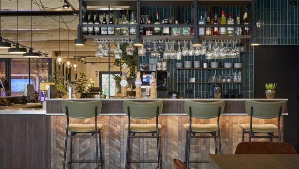 A bar area with a herringbone wood floor, bar stools, and a variety of bottles and glasses on shelves. - Comfy Bungalow near Bosland Nature Reserve (Hechtel-Eksel)