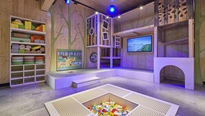 A children's play area with a large screen, wooden shelves with toys, and a play structure. - Comfy Bungalow near Bosland Nature Reserve (Hechtel-Eksel)