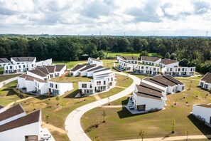 Et boligområde med moderne hvide huse, en snoet vej og en skov i baggrunden.