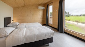 A bedroom with a large bed, wooden walls, and a window with a view of a field and a church. - Comfy Bungalow near Bosland Nature Reserve (Hechtel-Eksel)