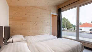 A bedroom with two beds, wooden walls, a large window, and a view of the outside.