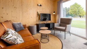 A modern living room with a wooden interior, a flat-screen TV, a sofa, a chair, and a small coffee table.