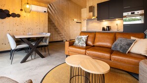 A modern interior with a wooden wall, a brown leather sofa, a dining table, and a kitchen area.