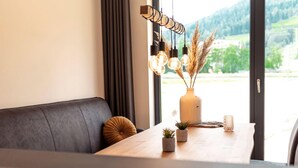 A modern dining area with a wooden table, a dark grey sofa, and a view of greenery outside. - Luxurious Apartment in St Georgen am Kreischberg With Sauna (Sankt Georgen am Kreischberg)