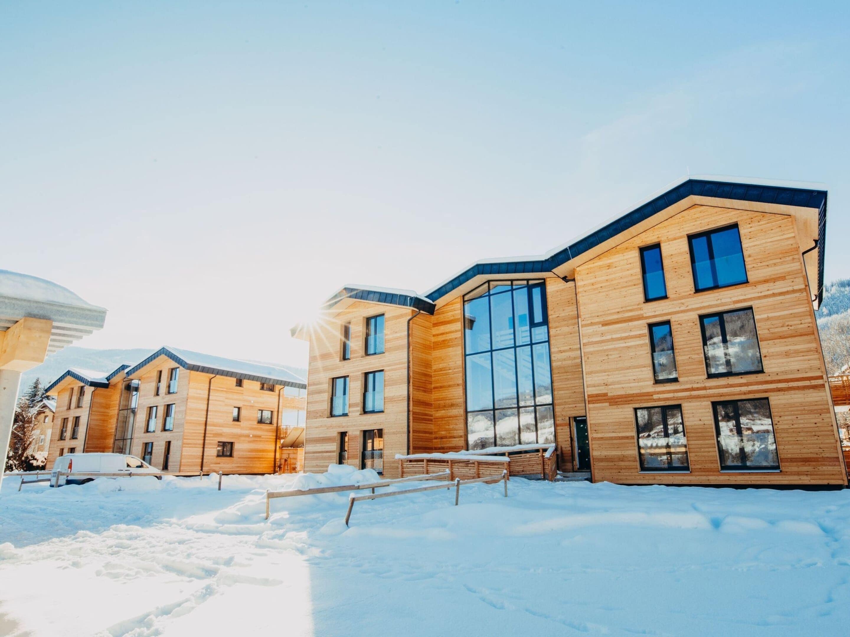 A modern multi-story building with large windows and a wooden facade, surrounded by snow.