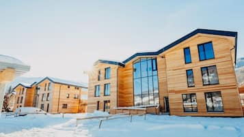 A modern multi-story building with large windows and a wooden facade, surrounded by snow.