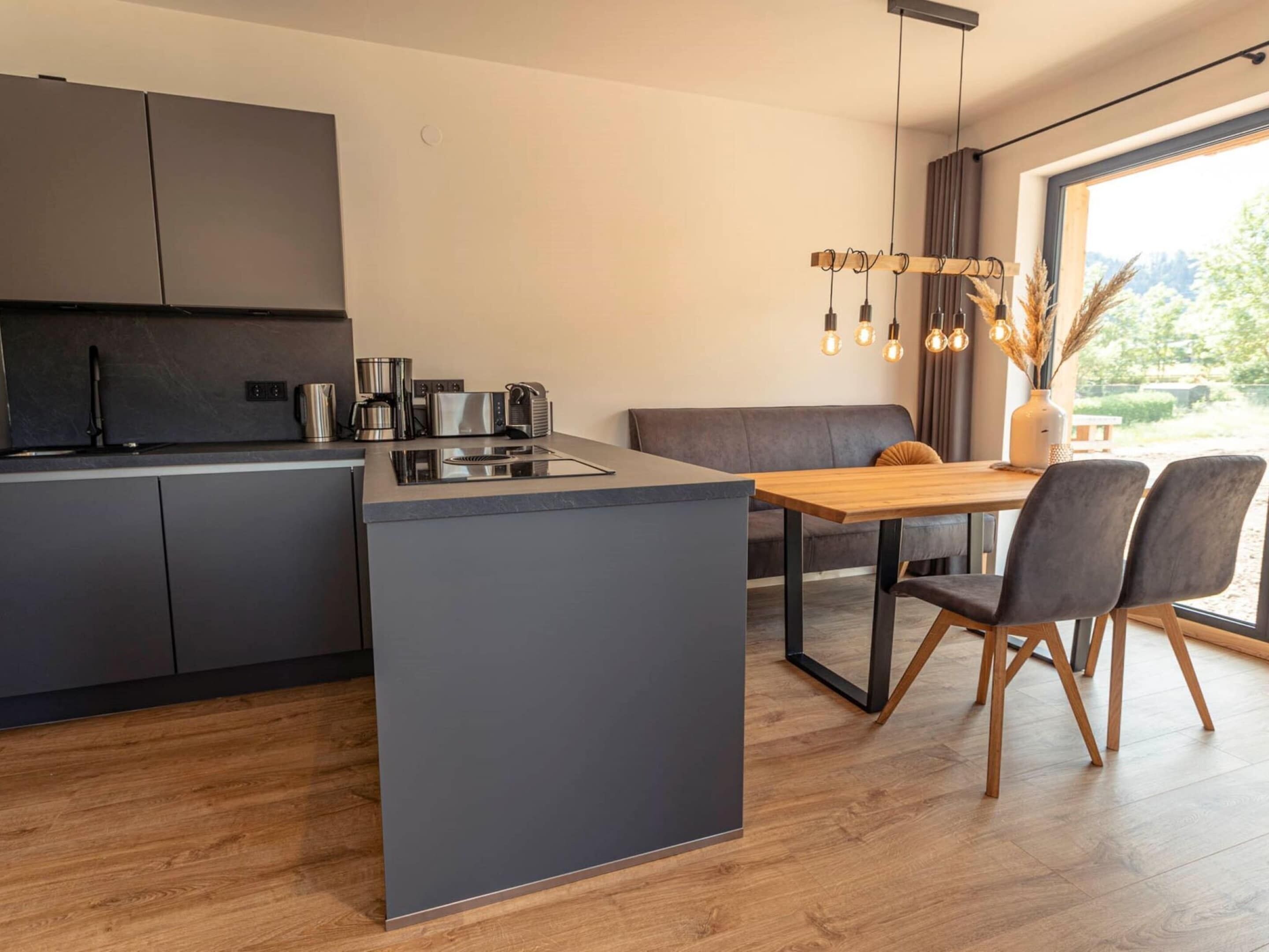 A modern kitchen with a central island, dark cabinets, and a dining area with a wooden table and chairs.