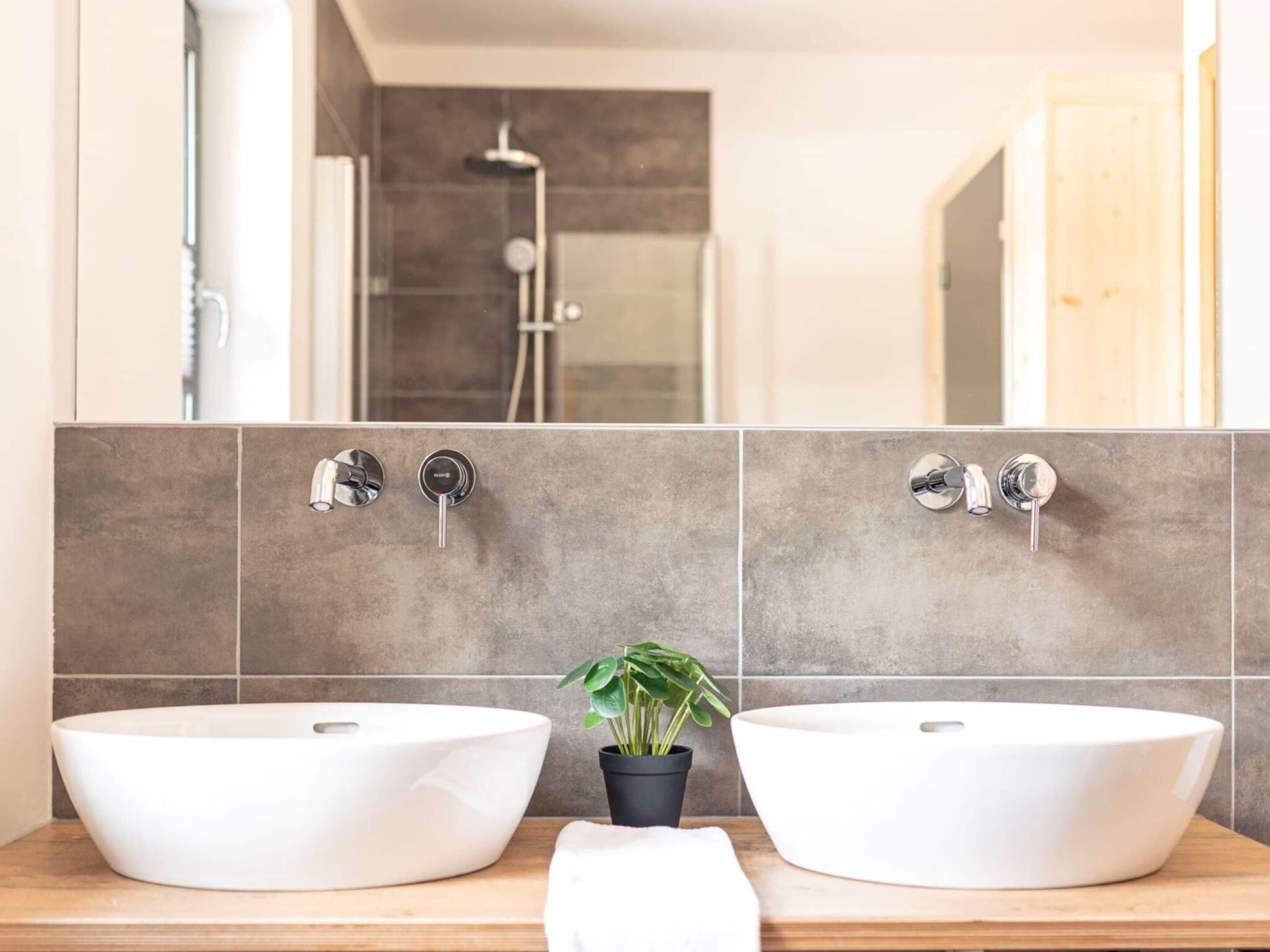 Un baño con dos lavamanos tipo cuenco blancos, una planta en maceta y una ducha a la vista.
