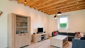 A modern living room with a wooden ceiling, a TV on a wooden stand, a grey sofa, and a cabinet with glassware.