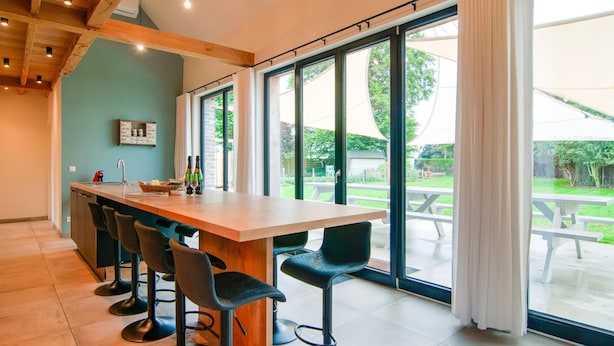 A modern kitchen with a large island, bar stools, and large windows offering a view of the garden.