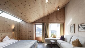 Una camera d'albergo moderna con soffitto in legno, un letto grande, un divano, un tavolino e vista sulle montagne dalla finestra.