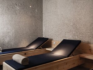Een wellnessruimte met twee houten ligbedden, een structuurwand en een klein tafeltje met een handdoek.
