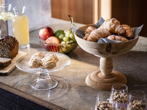 Een ontbijttafel met gebak, een fruitschaal en een brood op een marmeren aanrecht.
