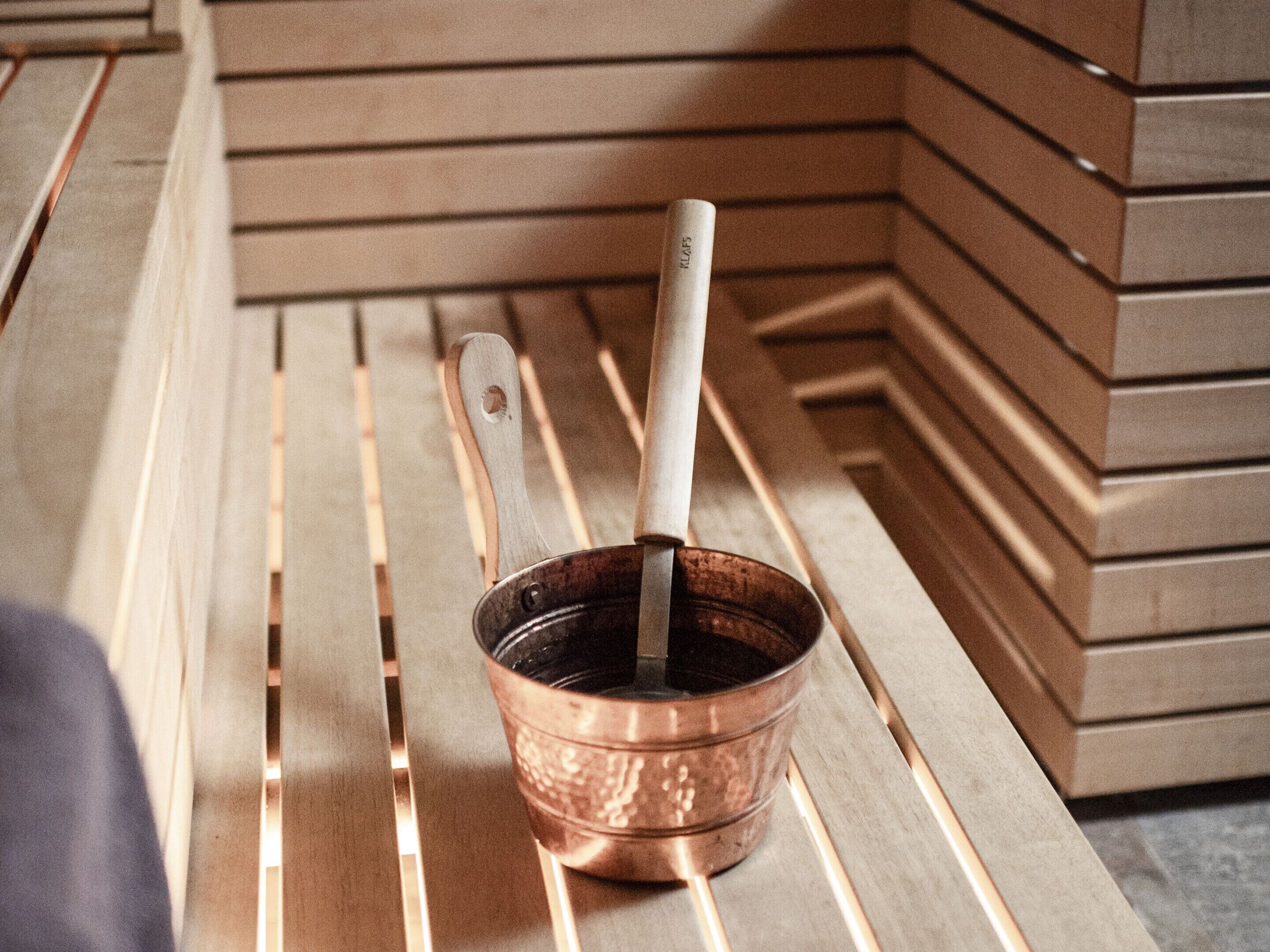 A copper mug with a wooden handle on a wooden bench.