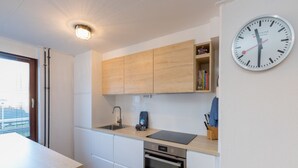 Une cuisine moderne avec des meubles en bois, un four encastré, un évier et une horloge au mur.