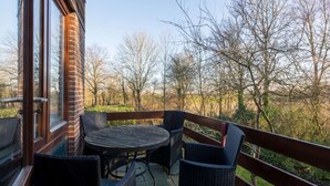 Un balcon agrémenté de meubles en osier, un mur en briques et une vue sur les arbres et l’herbe.