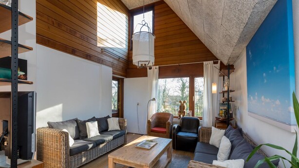 Un salon spacieux doté d’un haut plafond, de poutres en bois et de grandes fenêtres.