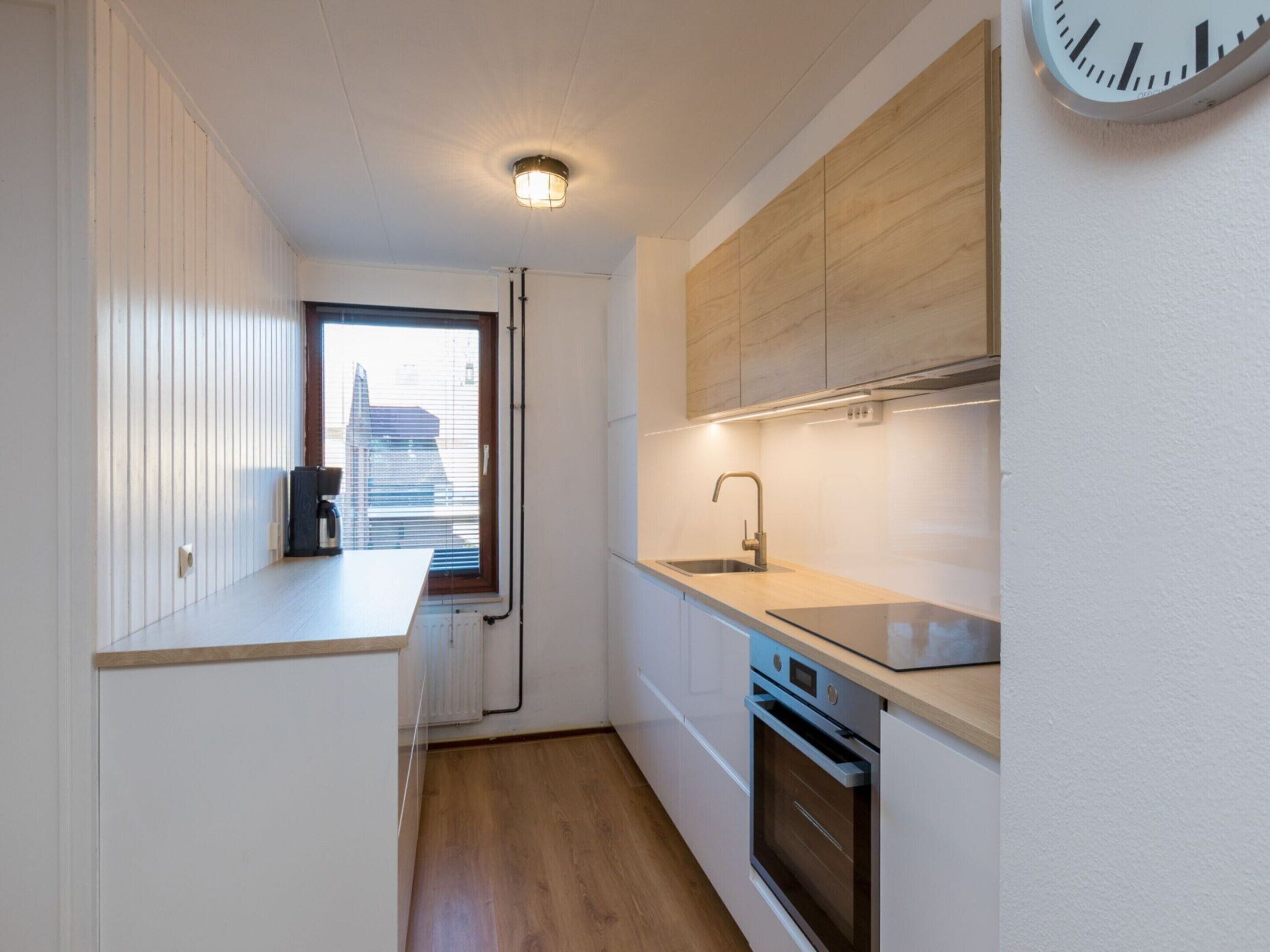Une cuisine moderne équipée d’un four encastré, d’un évier et d’une fenêtre avec des stores.