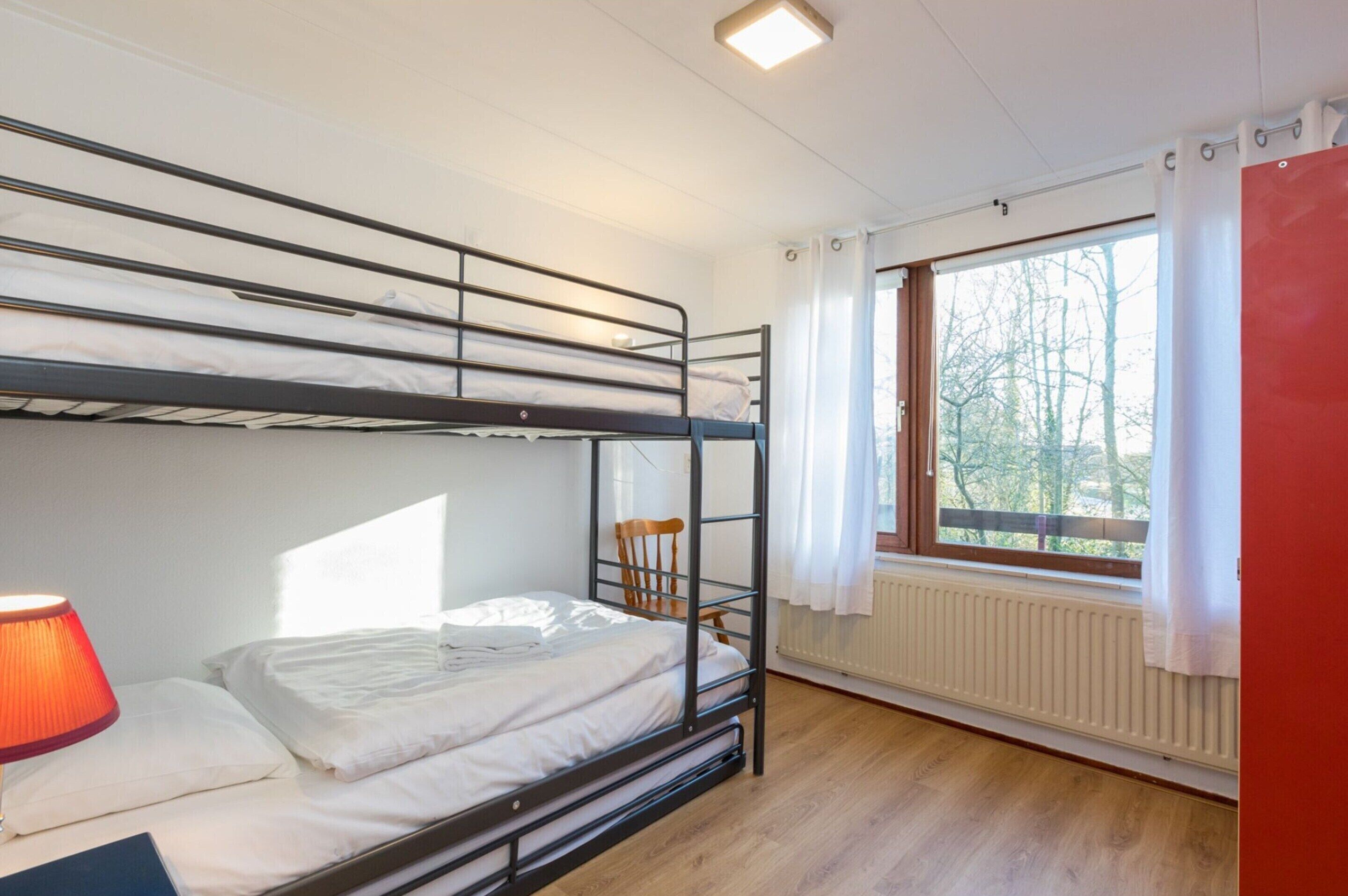 A bunk bed room with a radiator, a window with curtains, and a lamp.