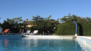 A clear swimming pool with lounge chairs and a building in the background. - Belvilla by OYO Aiolina (Sant'Angelo in Vado)