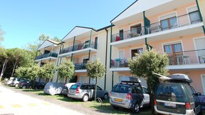 Une rangée d’immeubles d’habitation à deux étages, dotés de balcons, avec des voitures garées et des arbres.