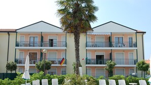 Un immeuble à plusieurs étages doté de balcons, d’un espace extérieur aménagé pour s’asseoir et d’un drapeau.