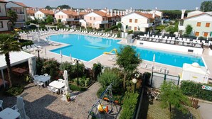 Une grande piscine entourée de chaises longues et de parasols, avec en arrière-plan la vue sur des immeubles résidentiels.