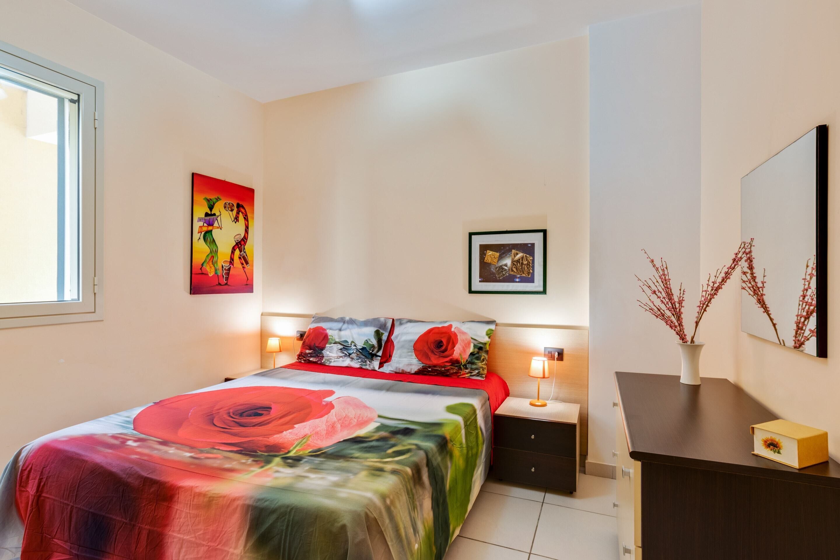 A bedroom with a bed, bedside tables, a dresser, and artwork on the walls.