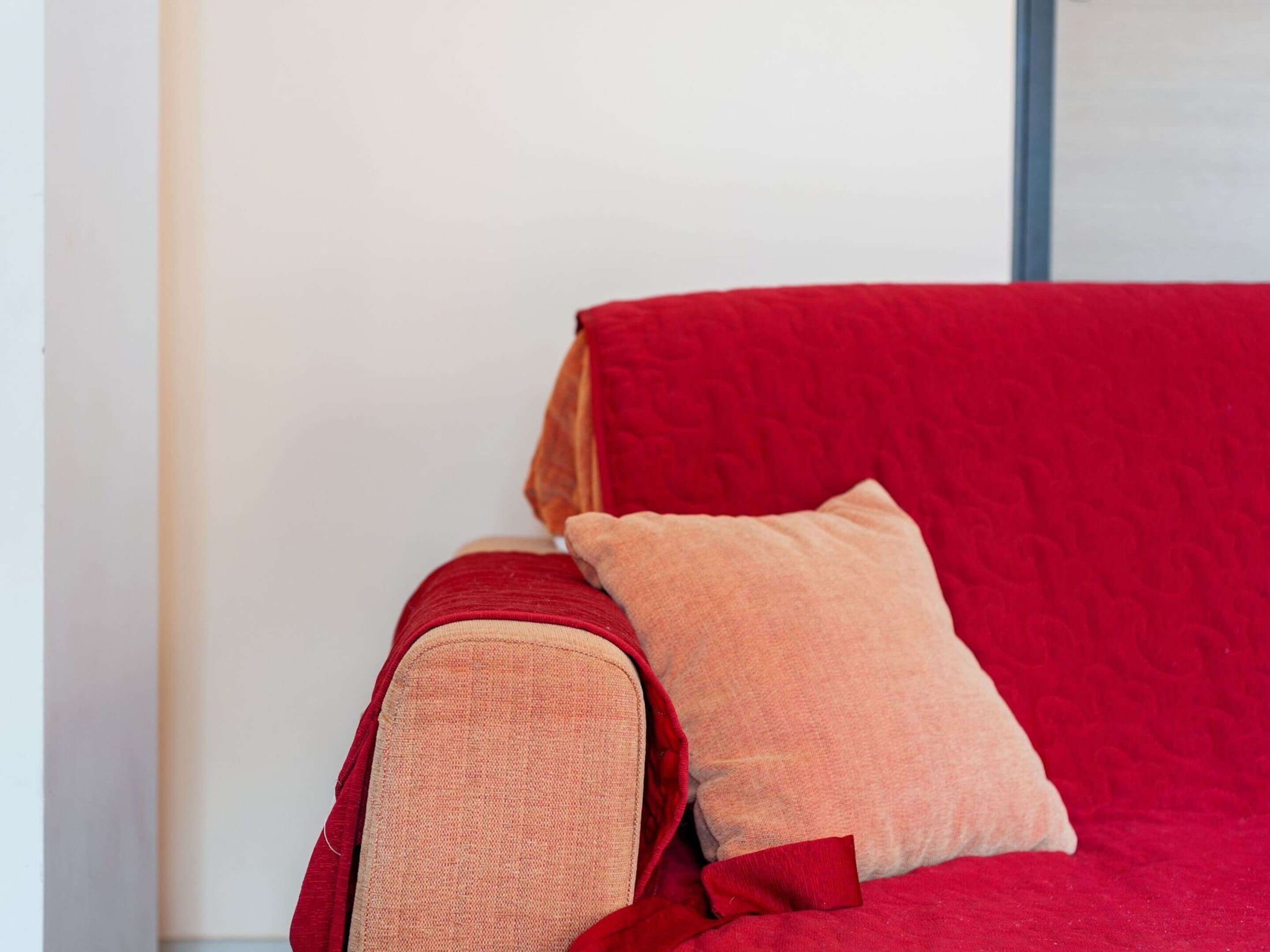 Un canapé rouge avec un coussin beige et un oreiller rouge.