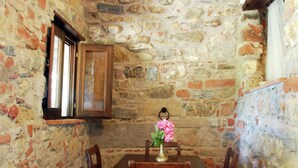 A rustic stone-walled room with a wooden table and chairs, a window with a wooden frame, and a vase with flowers on the table. - Villa in Velia Near Roman Ruins and Beach (Ascea)