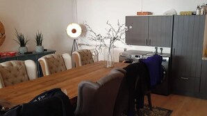 A dining area with a wooden table, upholstered chairs, a floor lamp, and a kitchen area with cabinets and appliances.