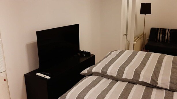 A hotel room with a bed, a TV on a stand, a bedside table, and a floor lamp.