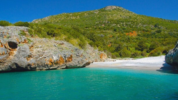 A coastal landscape with a rocky shoreline, clear turquoise waters, and a hill with sparse vegetation. - Romantic Stay Near Velia (Ascea)