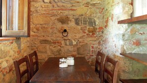 A rustic dining area with a wooden table and chairs, a stone wall, and a wooden shelf. - Romantic Stay Near Velia (Ascea)
