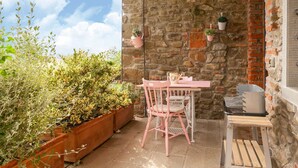A stone-walled patio with a table and chairs, potted plants, and a grill. - Belvilla by OYO Il Nido (Castelfranco Piandisco)