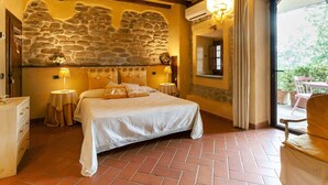 A bedroom with a stone wall, a bed with white linens, a wooden ceiling, and a view of the outdoors. - Belvilla by OYO Il Nido (Castelfranco Piandisco)