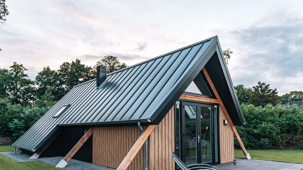 Une maison moderne avec un toit en pente, un revêtement extérieur en bois et une porte d’entrée en verre.